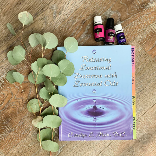 Releasing Emotional Blocks With Essential Oils book and Young Living essential oils with leaves on a wood backdrop